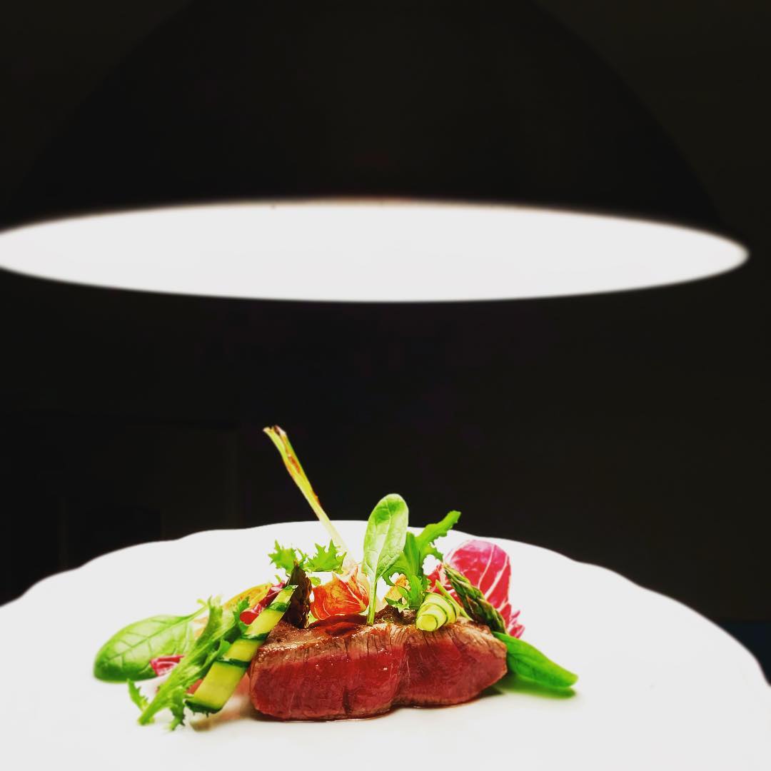Dramatic plated meat dish under an overhead light.