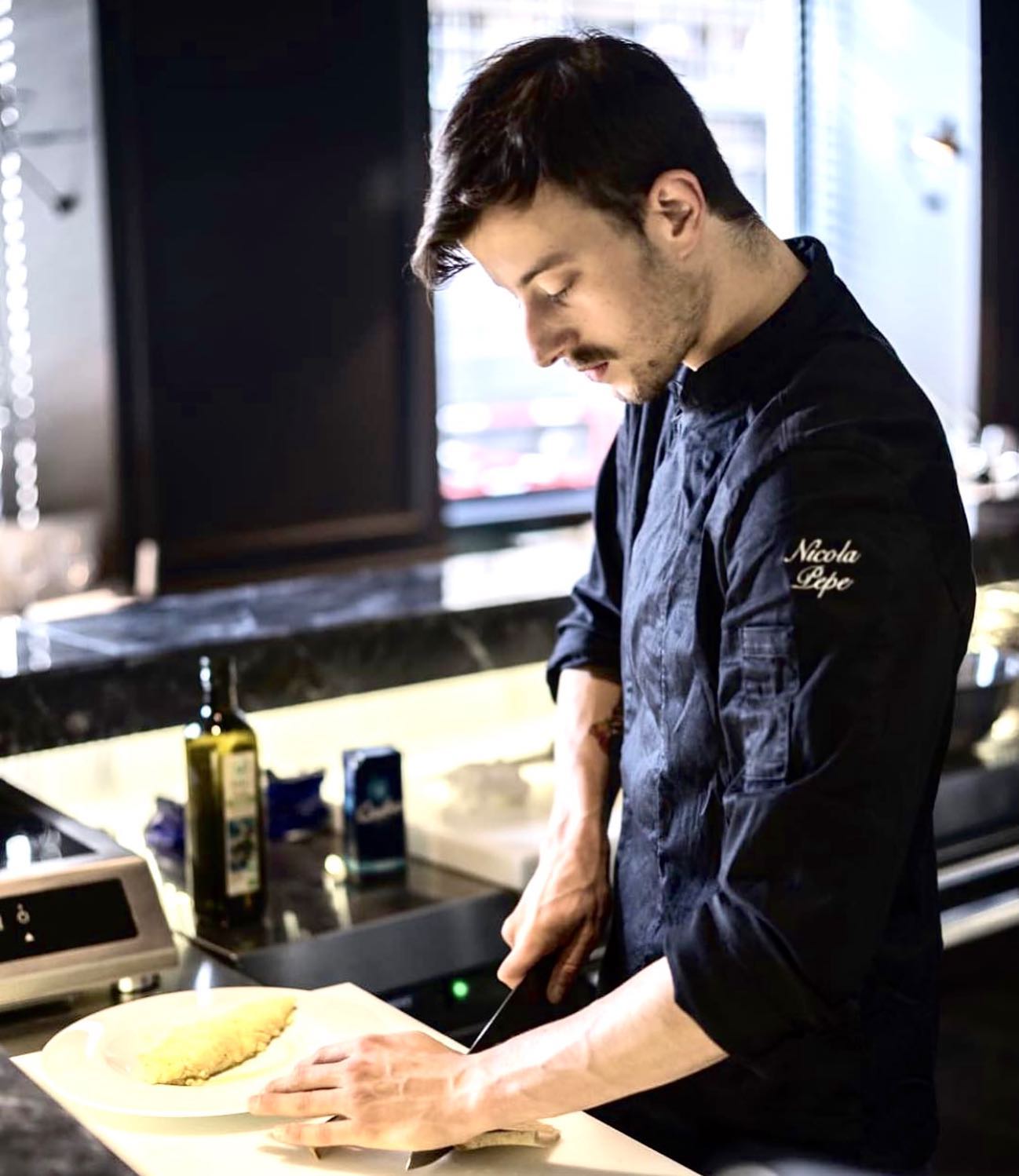 Nicola Pepe working at a kitchen counter in a black chef coat.